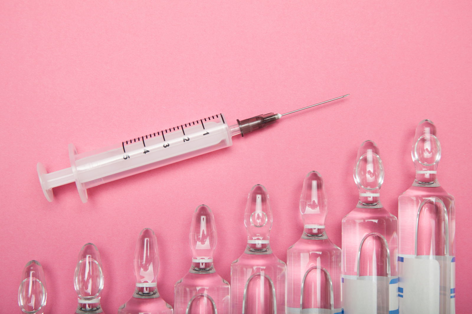 Increasing dependence on injections of hyaluronic acid, botox and collagen. Syringe and ampoules on a pink background.