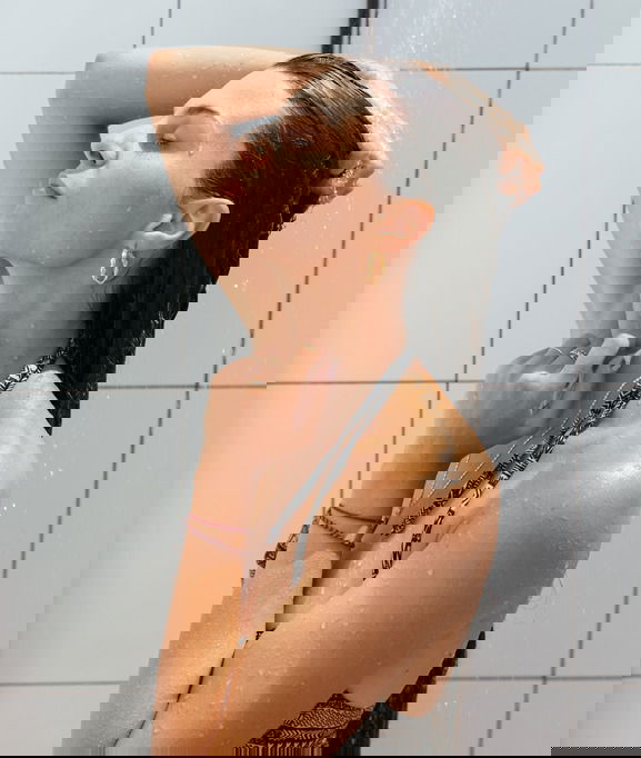 Young woman in swimsuit showering at outdoor shower. conditioner hair mask microblading