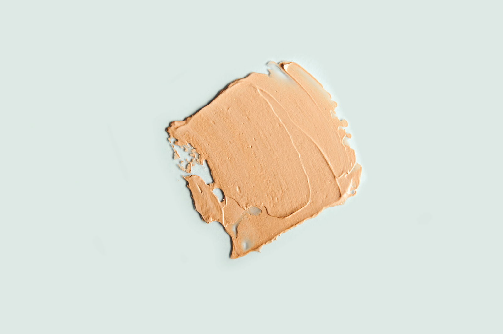Facial concealer strokes BB or CC cream foundation on light blue background. Close-up of liquid foundation, texture of a makeup product.
