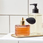 Trendy arrangement of crystal bottles with perfume and various beauty products on white tiled surface