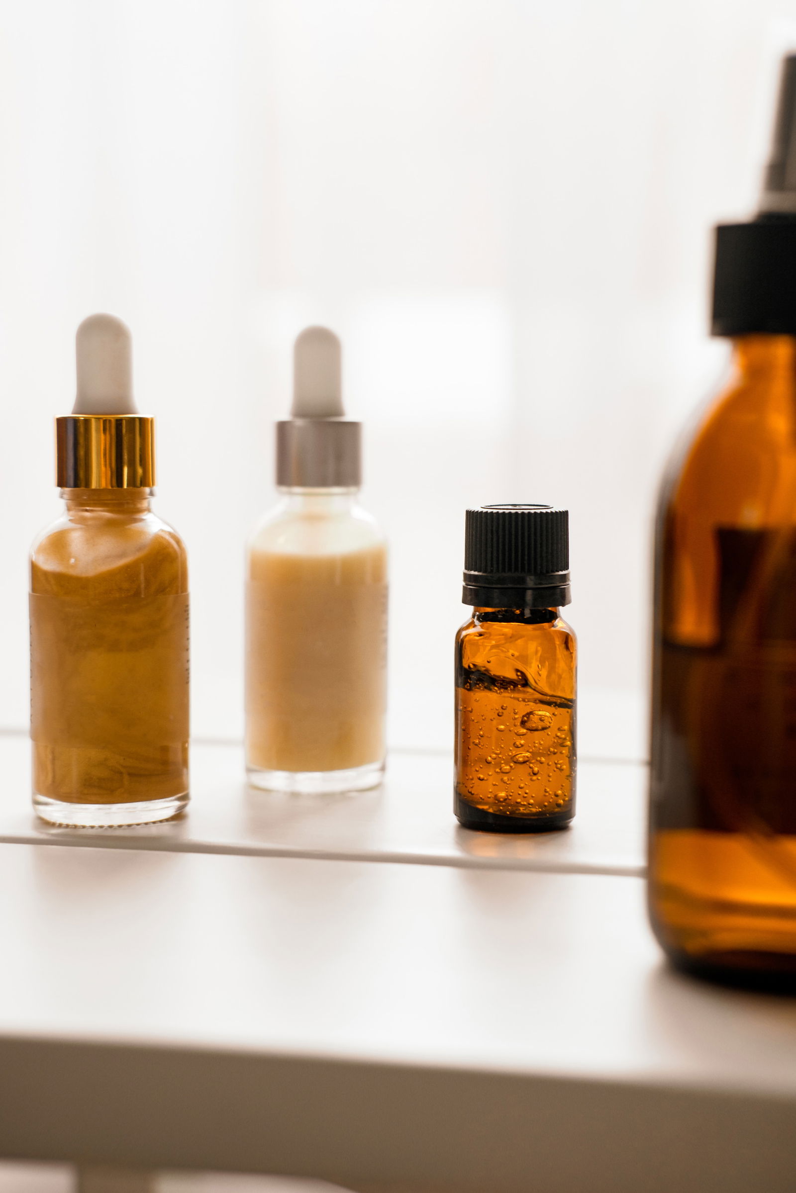 Glass bottles with dropper pipettes. Luminous and luxury gold and white liquid highlighter drops. Beauty blogger essentials. Minimalism package, branding mockup. Direct sun light