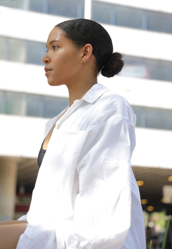 outdoor portrait of a young black female, wearing a white shirt, in profile low bun hairstyle