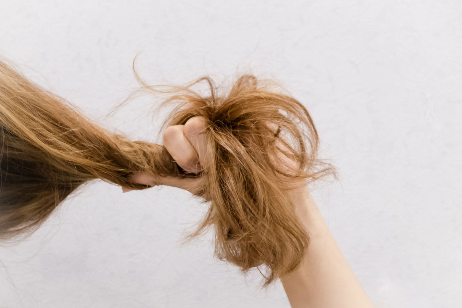 Woman with dry hair checking the health of her hair before doing a bleach shampoo