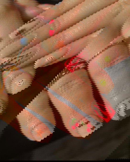 Natural nails with red and orange mismatched designs and smiley faces