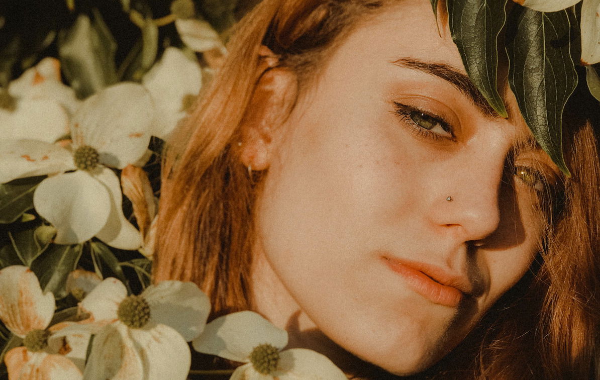 Portrait of young woman with red hair surrounded by tree leaves summer autumn tan